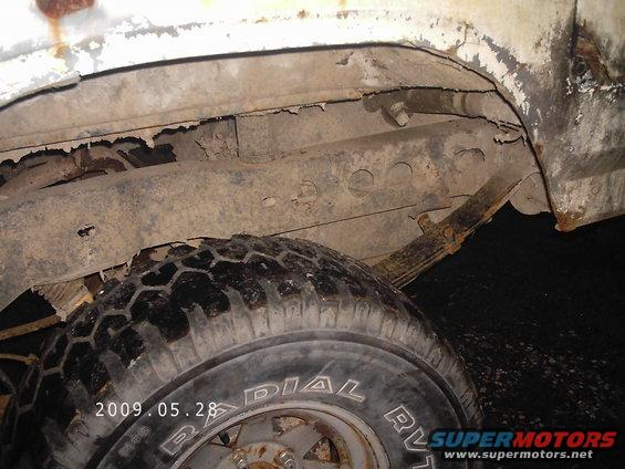 Close-up of a rusty frame, leaf spring, and tire on an old vehicle