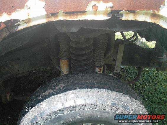Rusty front wheel well with exposed suspension components and a worn tire