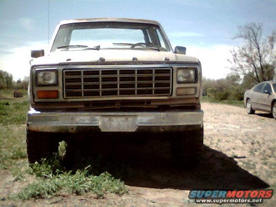 Front view of a 1980s Ford pickup truck with a chrome bumper and grille. Another car is visible in the background