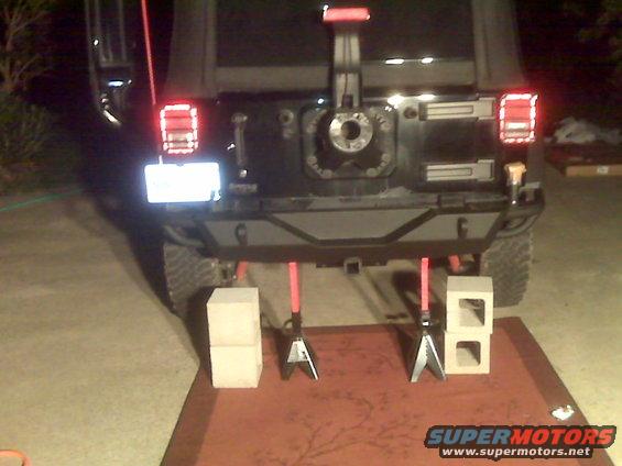 Rear of black 2007 Jeep Wrangler with aftermarket bumper and tire carrier, on jack stands