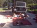 2008 Jeep Wrangler - Two people are working on the underside of a Jeep Wrangler in a driveway, with another Jeep parked behind it.