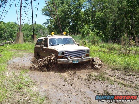 Brown Ford Bronco splashing through a muddy trail near power lines