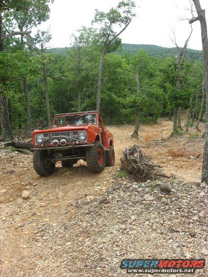 Orange SUV with off-road tires and a brush guard on a dirt path in the woods
