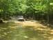 1987 Suzuki Samurai - Two off-road vehicles navigate a muddy water crossing surrounded by dense forest.