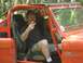 1987 Suzuki Samurai - A man sits in the driver's seat of an orange off-road vehicle, holding up two fingers in a peace sign.