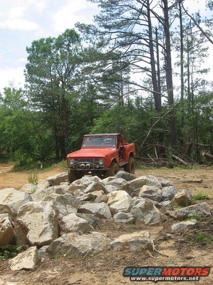 Orange off-road vehicle with a roll cage, driving over large rocks