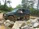 1987 Suzuki Samurai - Jeep Grand Cherokee tackling a rocky off-road course with a driver looking out the window.