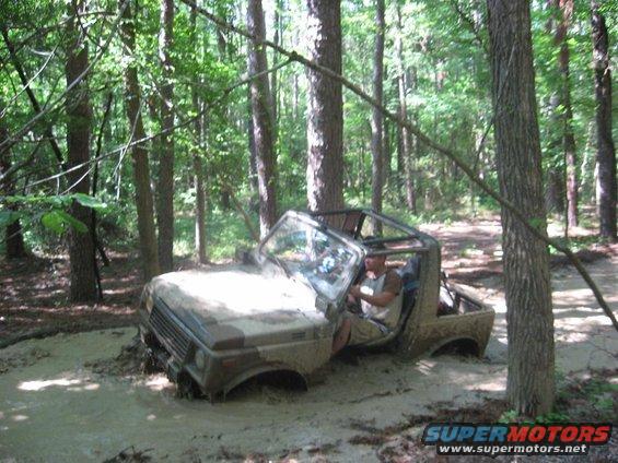 Camouflaged Suzuki Samurai stuck in mud, front-left wheel submerged