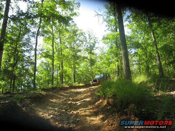 Off-road vehicle driving up a rocky dirt path through a forest