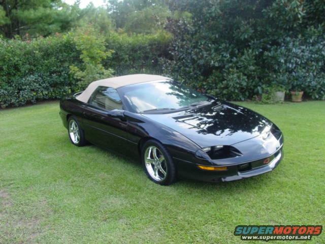 Black convertible with tan top parked on grass, front 3/4 view. Chrome wheels. Supermotors.net logo in lower right