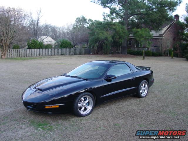 Black Pontiac Firebird parked on a grassy lawn in front of a house