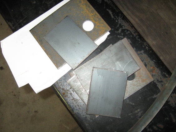 Stack of various sized metal plates, some with rust, on a dark surface