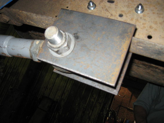 Close-up of a custom metal bracket bolted to a rusty vehicle frame, with a grey pipe attached