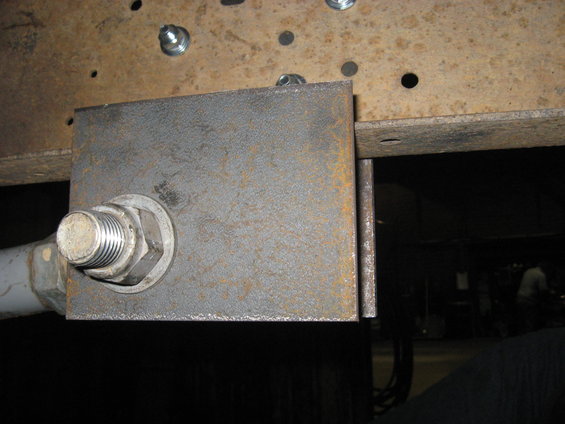 Close-up of a metal plate bolted to a vehicle's frame with a large bolt and nut. Some holes are visible in the frame above