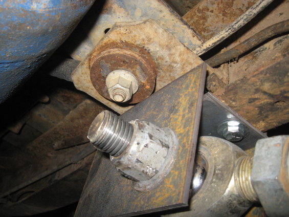 Close-up of a rusted metal bracket with bolts and nuts attached to a vehicle's undercarriage