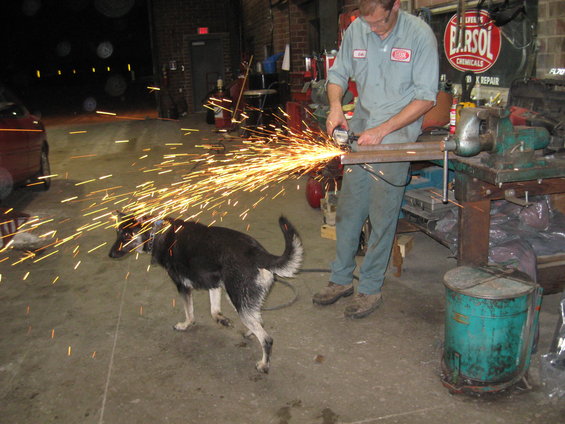 Dog watches mechanic grind metal in a workshop