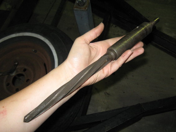 Hand holding a tapered reamer tool with a hexagonal shaft and a pointed tip