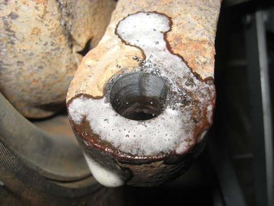 Rusted metal part with a hole, covered in foam and dripping