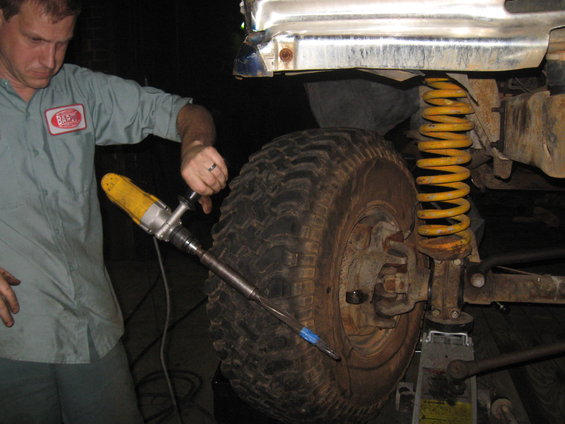 guy working on suspension of lifted off-road vehicle, using a tool on the wheel hub