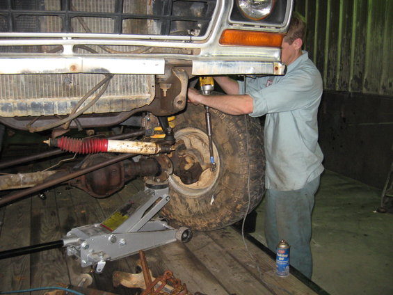 1978 Ford Bronco front wheel assembly with a man using a drill, jack supporting the vehicle