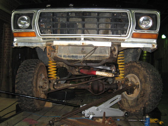 1978 Ford Bronco front end with chrome grille, orange turn signals, and yellow suspension springs. The vehicle is on a jack