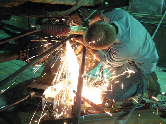 Man welding under vehicle chassis, sparks flying