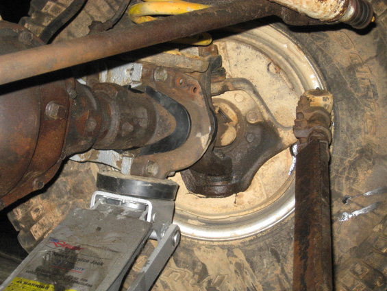 Close-up of vehicle's rear axle, suspension components, and a floor jack lifting the frame