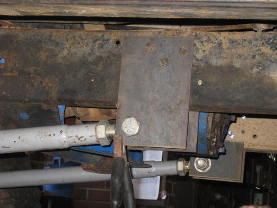 Close-up of a metal bracket bolted to a rusty vehicle frame, with suspension components visible
