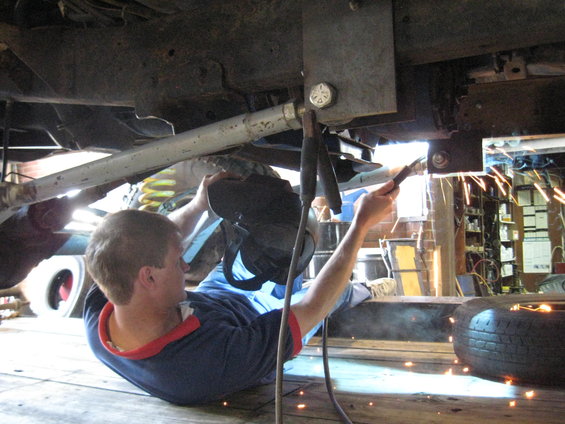 Person welding under a vehicle's frame. Sparks fly as they work