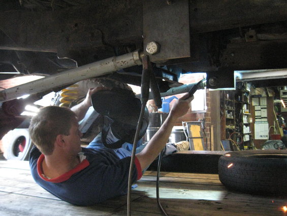guy welding under a vehicle, spare tire nearby