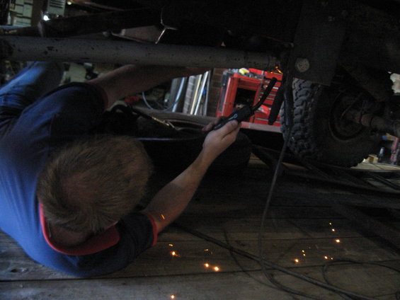 Person welding under a vehicle chassis, with a tire visible