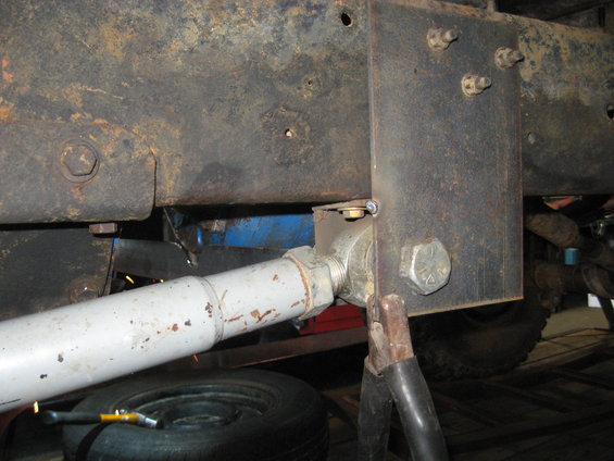 Close-up of rusty truck frame with a shock absorber and suspension linkage attached. A tire is visible below
