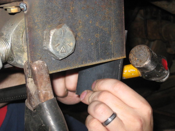 Close-up of a metal part with a bolt and clamp, hands working on it