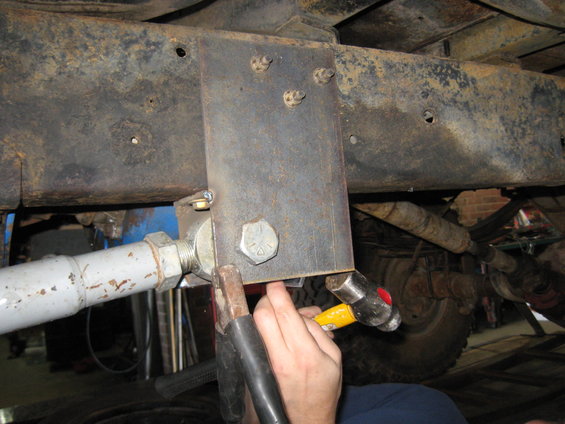 Close-up of a metal bracket being attached to a rusty vehicle frame with bolts and a hammer