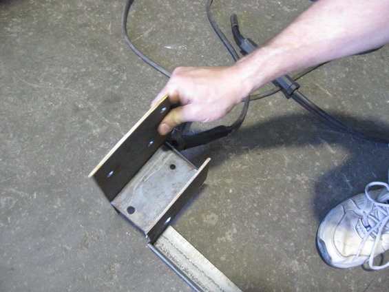 Hand holding metal bracket with welding cable and shoe in background