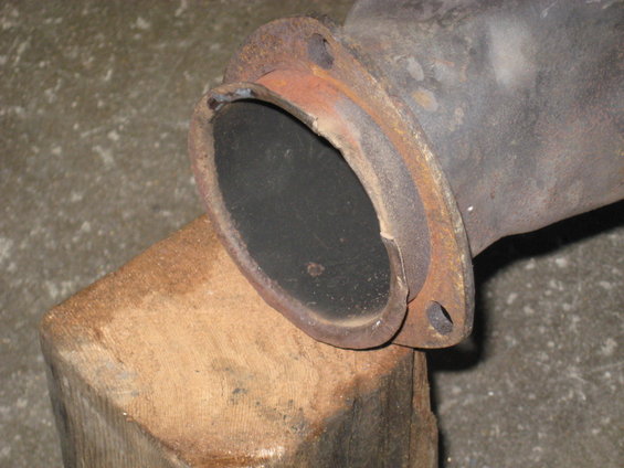 Close-up of a rusty exhaust pipe flange resting on a wooden block