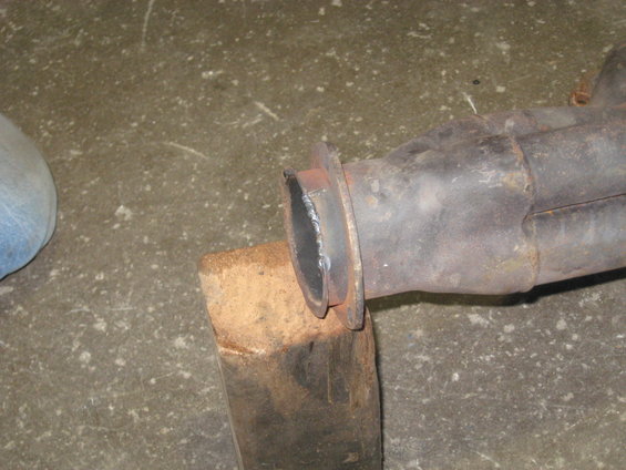 Exhaust pipe flange with weld marks, supported by a wooden block