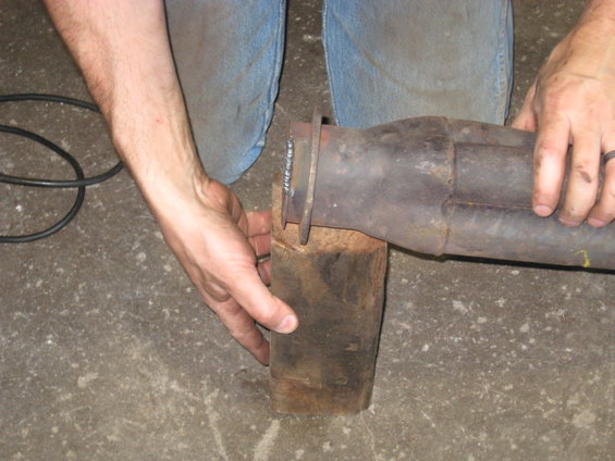 Exhaust pipe section held by hands over wooden block