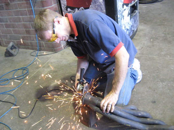 Man in blue shirt and jeans grinding an exhaust pipe with sparks flying