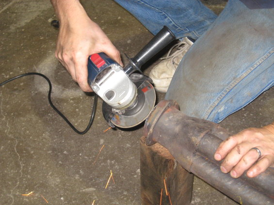 Exhaust pipe section being cut with an angle grinder, sparks flying