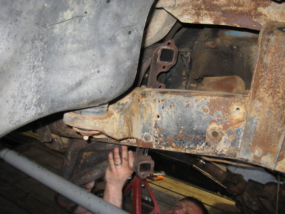 Rusty vehicle frame with exhaust manifold and a person's hands working on it