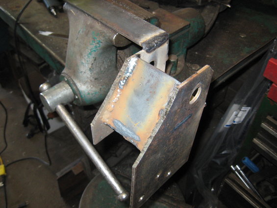 Welded metal bracket held in a green vise