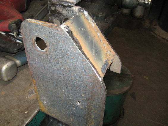 Close-up of a rusty, welded metal bracket with a hole in it, resting on a workbench