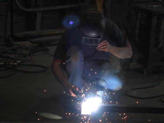 Welder in a helmet and jeans sparks metal with a welding torch