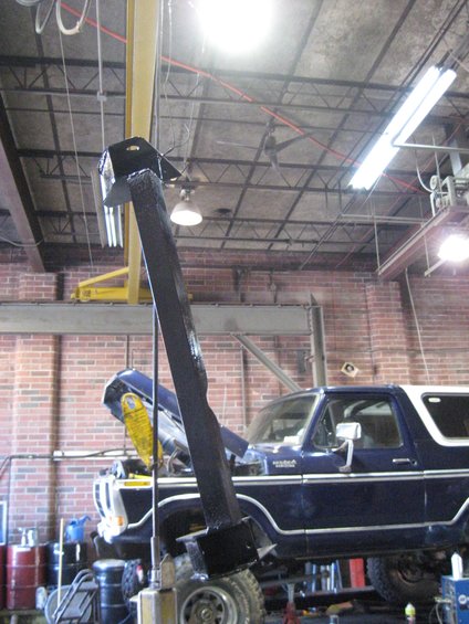 Dark blue Ford Bronco with a white top, hood up, in a garage with a lift
