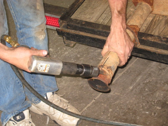 Man using a tool on a rusty exhaust pipe section on a trailer