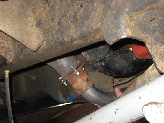 underneath view of a vehicle's exhaust pipe being worked on, with rusty frame and blue painted parts visible