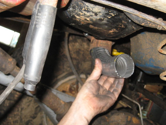 Hand holding a bent metal exhaust pipe section near vehicle undercarriage