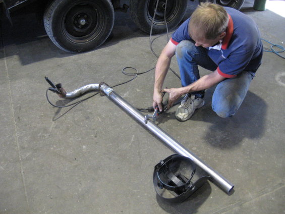 Man welding an exhaust pipe with a welding mask on the ground