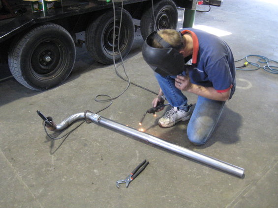 Man in welding mask and jeans working on exhaust pipe on concrete floor